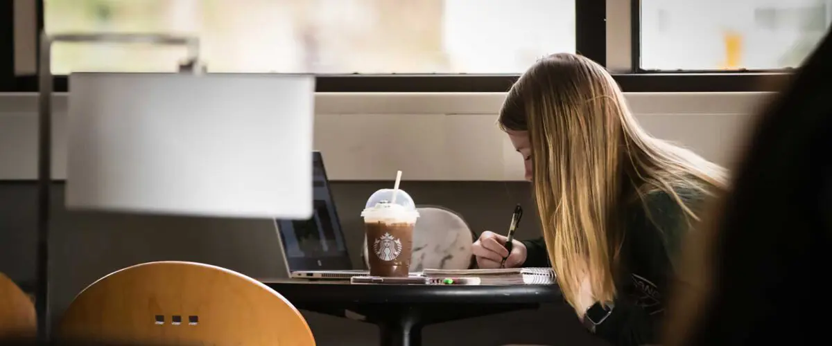 Student studying at table with iced coffee beverage is centered on screen