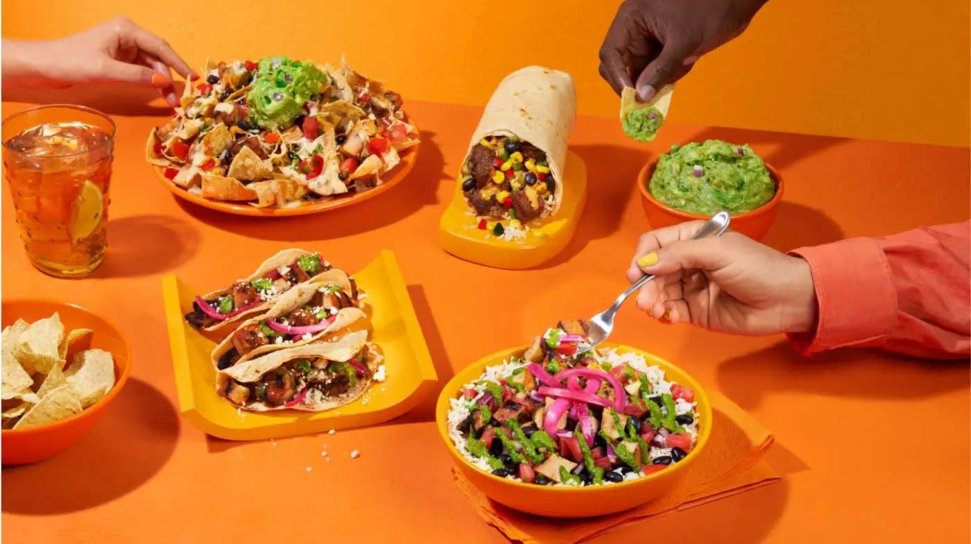 Assorted menu items on orange table with hands reaching